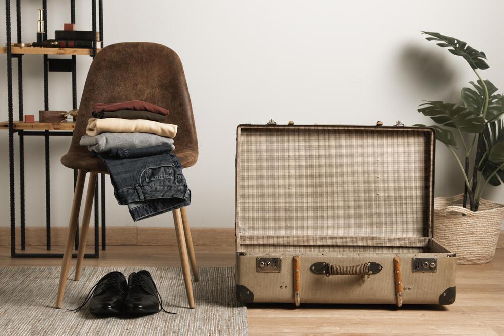 Un banco de madera está acompañado de una maleta vintage abierta, decorada con ropa doblada y una planta, evocando un estilo retro que combina funcionalidad y estética en un espacio cálido y acogedor.