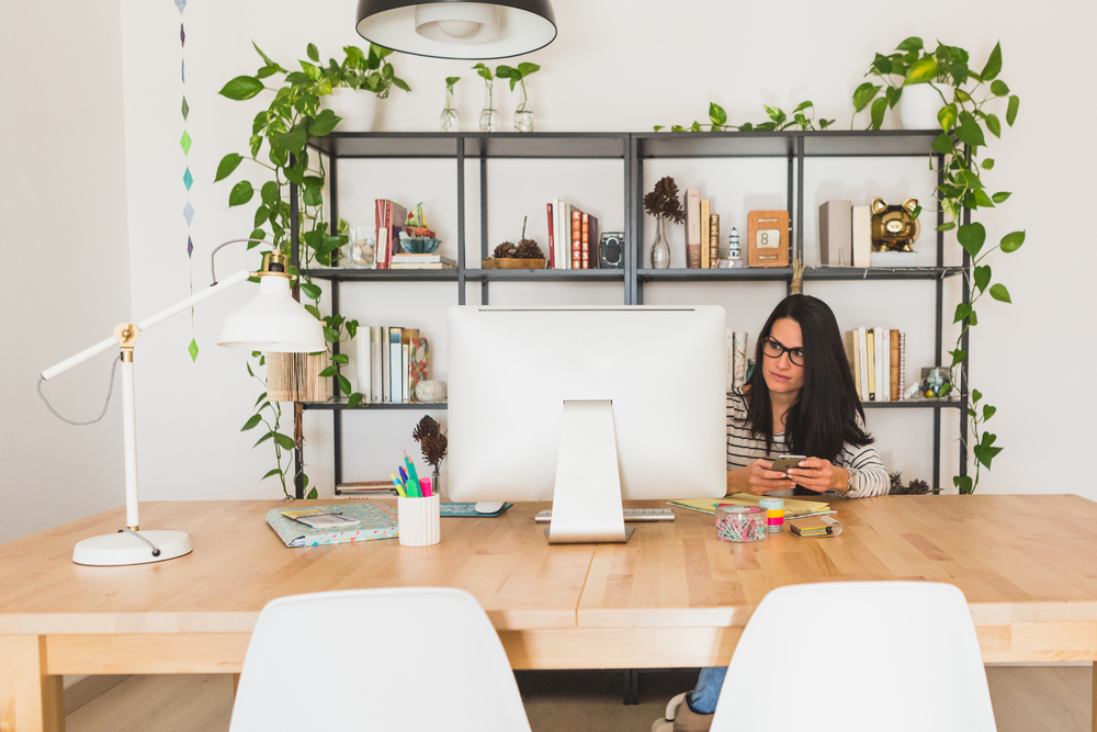 En este despacho contemporáneo, una mujer trabaja en un ambiente agradable y funcional. El espacio destaca por su diseño ergonómico, con un escritorio de madera, una lámpara de escritorio y plantas decorativas que aportan frescura y un toque personal, ideal para fomentar la productividad y el bienestar.