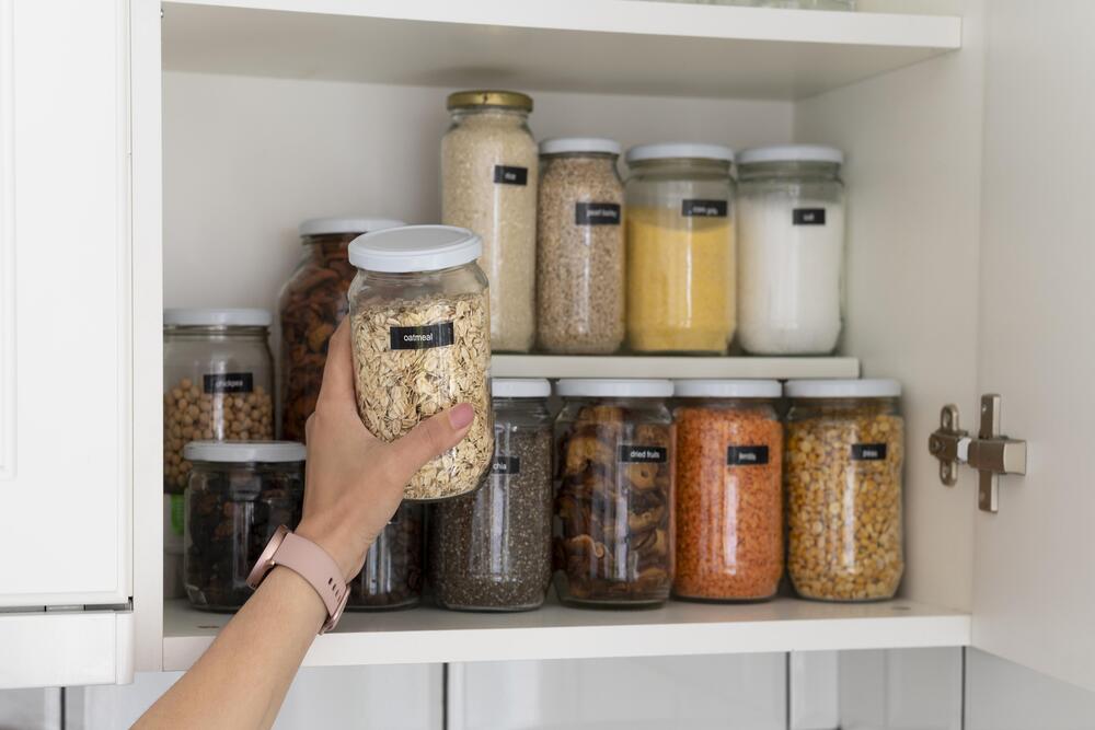 Vista detallada de un armario de cocina bien organizado, donde se observan frascos de vidrio etiquetados con especias y granos, resaltando la importancia de la organización en la cocina.