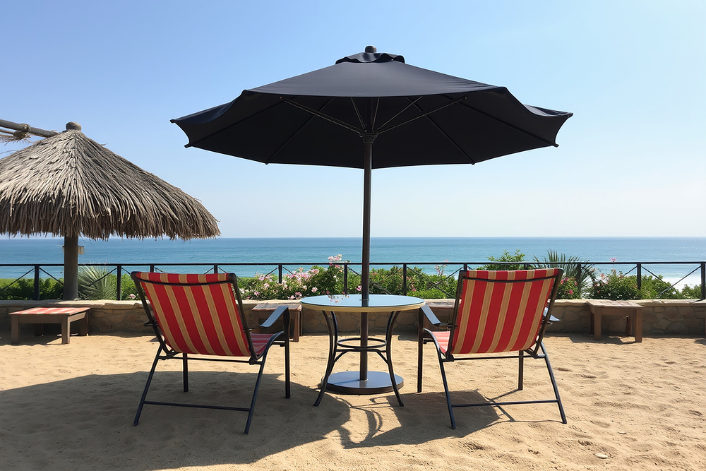 Espacio de descanso en la playa con tumbonas y una sombrilla negra, ideal para disfrutar del sol mientras se protege del calor. La imagen refleja un ambiente relajante junto al mar.