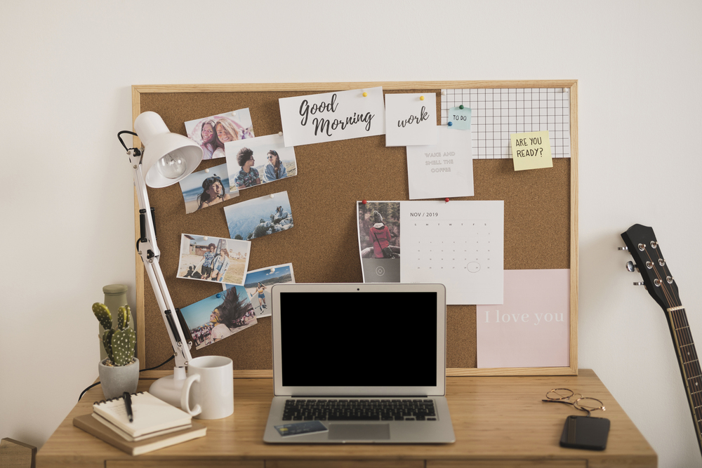 Un espacio de oficina en casa bien organizado, con un tablero de corcho que muestra fotografías y recordatorios, un ordenador portátil en una mesa de madera y elementos decorativos como una planta, creando un ambiente inspirador y productivo.