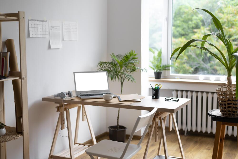 Vista de un escritorio bien iluminado, equipado con una computadora portátil y decoración de plantas, ideal para un espacio de estudio funcional y acogedor.