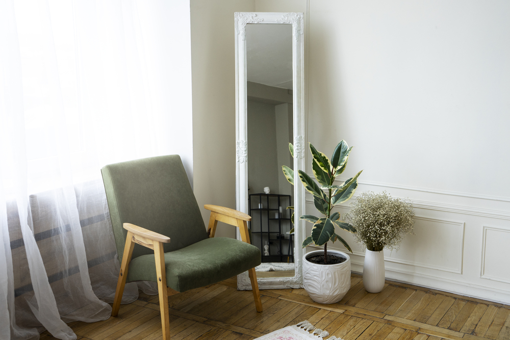 Espacio decorativo que incluye un sillón verde y un espejo de cuerpo entero, rodeado de plantas, ideal para fomentar una atmósfera armoniosa y luminosa.