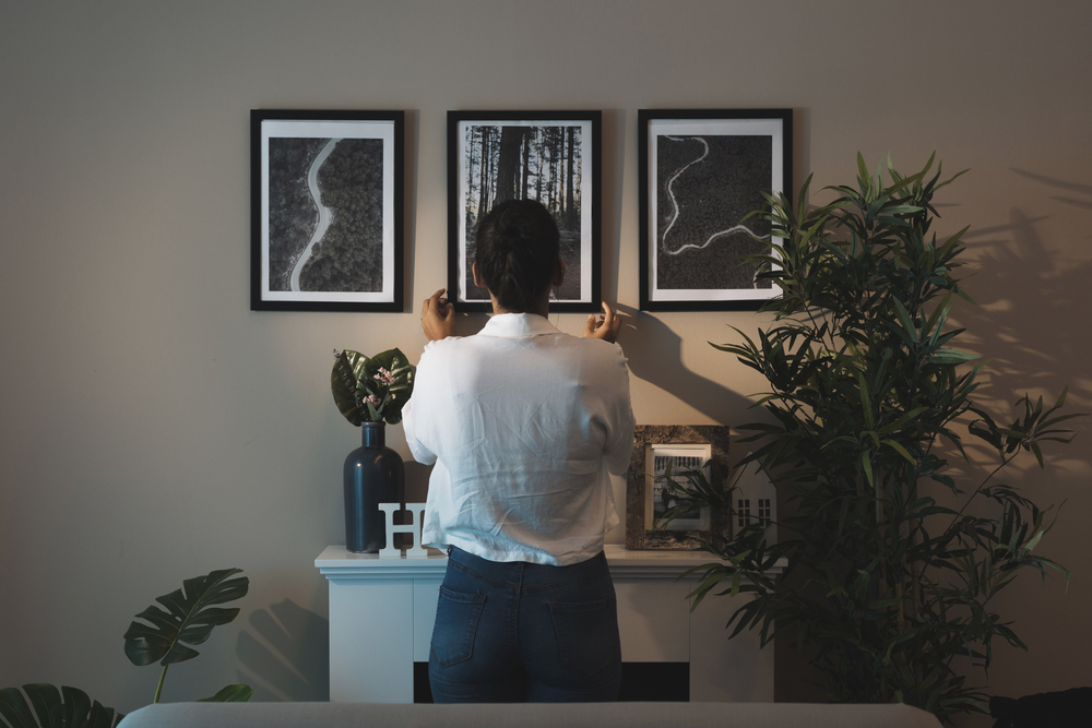Una persona coloca cuidadosamente cuadros en la pared de su hogar, creando una exhibición artística. La combinación de decoración minimalista y elementos naturales agrega calidez y estilo al ambiente.