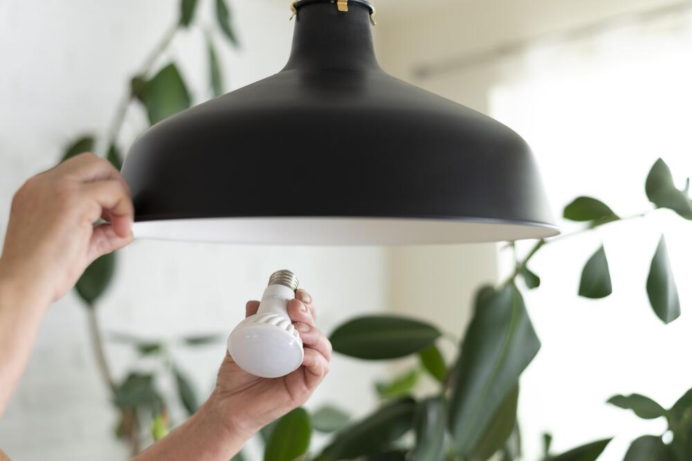 Instalación de una bombilla LED en una lámpara moderna, enfocada en la sostenibilidad y el bienestar en espacios interiores.