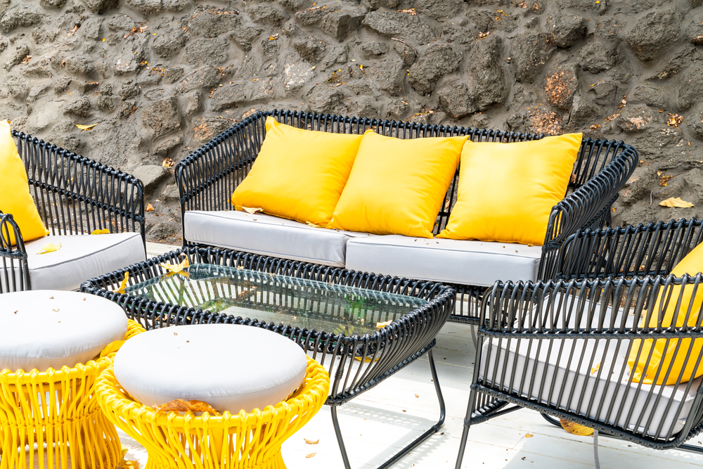 Un atractivo conjunto de muebles de terraza presenta un sofá de cuerda negra con cojines amarillos brillantes, rodeado de una mesa de vidrio. El diseño contemporáneo y vibrante añade un toque de frescura al espacio exterior, ideal para relajarse y disfrutar del aire libre.