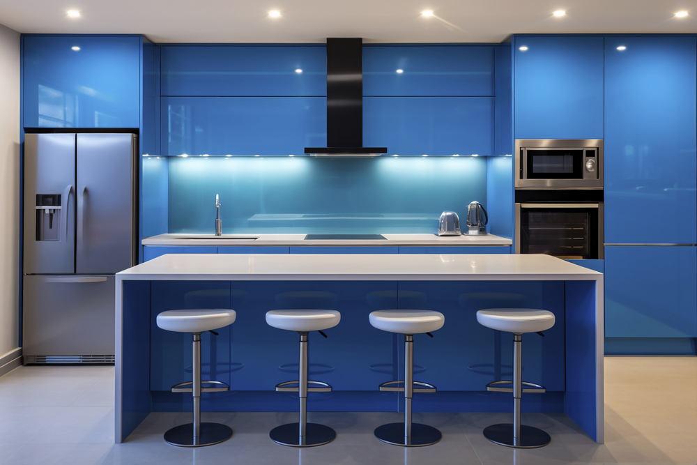 Cocina contemporánea con una estética fresca, caracterizada por sus armarios y encimeras en azul brillante, complementada con una barra blanca y sillas altas, ideal para un ambiente dinámico y acogedor.